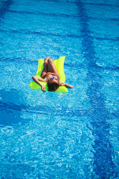 Jeune homme sexy en maillot de bain nage dans la piscine sur un matelas gonflable. Fille en lunettes de soleil dans une piscine bleue en vacances - Photo, image
