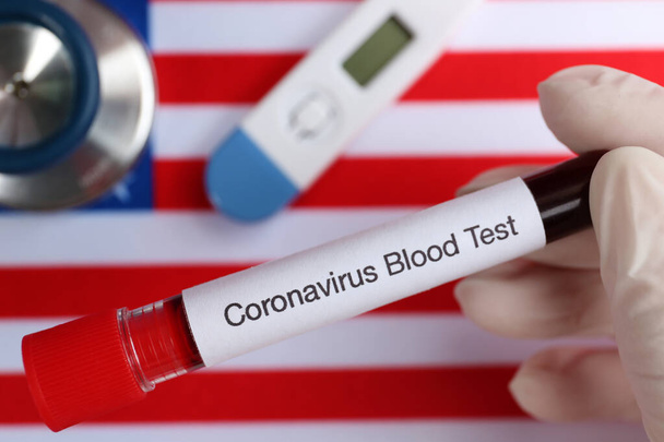 Scientist holding test tube with blood sample over American flag, closeup. Coronavirus pandemic in USA - Fotografie, Obrázek