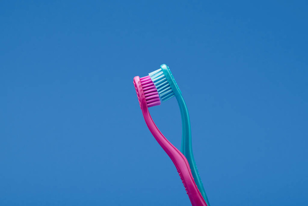 Cepillos de dientes rosados y azules dispuestos como pareja besándose para una idea de concepto mínima sobre el concepto de fondo azul - Foto, Imagen
