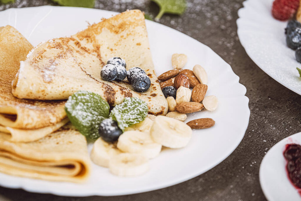 Pancakes with nuts, blueberries, banana and mint leaves. Close-up on a served plate with sweet dessert. - 写真・画像