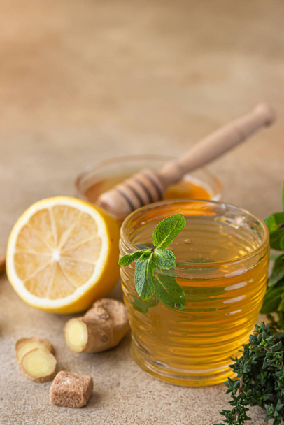 Hot mint and thyme tea with ginger root, lemon and honey, light concrete background. Herbal tea. - Photo, image