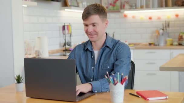 Nuori mies freelancer opiskelija käyttää kannettavaa tietokonetta opiskelee verkossa työskentelevät kotoa internetissä, hymyillen keskittynyt tuhatvuotinen kaveri kirjoittamalla tietokoneella surffailu web katselee näytön nauttia etäinen työ - Materiaali, video