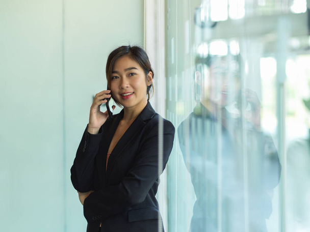 Retrato de la mujer de negocios hablando por teléfono mientras está de pie en la sala de oficina de partición de vidrio - Foto, Imagen