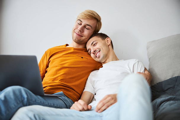 Feliz casal homossexual abraçando e usando laptop em casa - Foto, Imagem