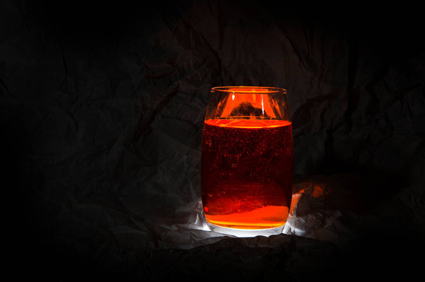Un vaso, una pila di liquido ambrato con riflessi e tinte di luce su fondo scuro - Foto, immagini