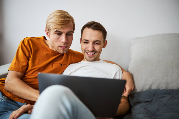 Hermosa pareja homosexual usando un portátil moderno en casa - Foto, imagen