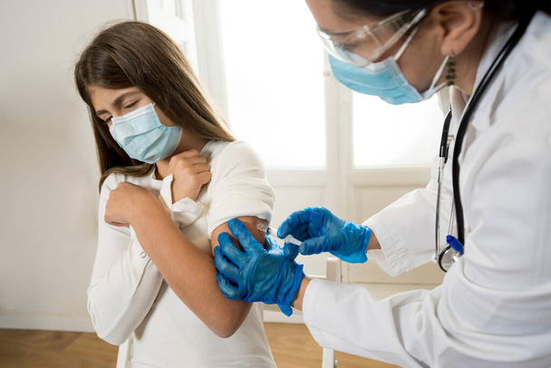 Nurse administering the coronavirus vaccine to a a young girl patient with face mask in Doctors clinic. Immunization, medical treatment and Covid-19 vaccination program after clinical trial in humans. - Foto, Imagem