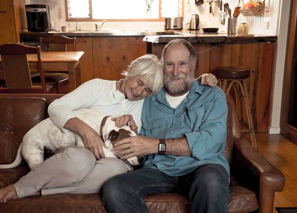 Confident senior couple relaxing and loving their cute pet dog enjoying life at home together. Positive image of coronavirus Outbreak Stay Safe and animal benefits for mental health Concept. - Фото, зображення