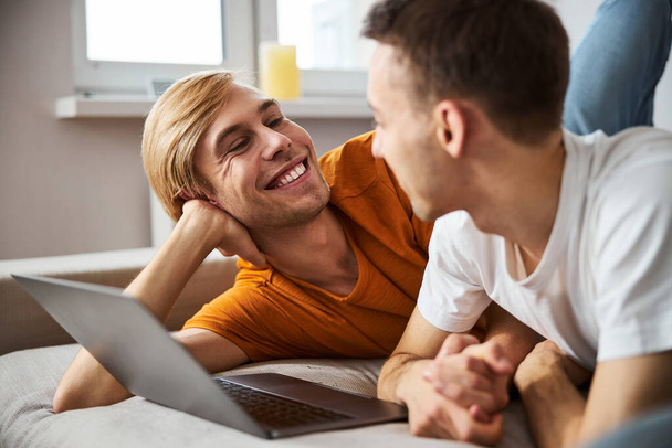 Happy gay couple spending time together and using notebook at home - 写真・画像