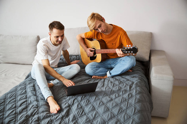 Красивий чоловік грає на гітарі, проводячи час з хлопцем вдома
 - Фото, зображення