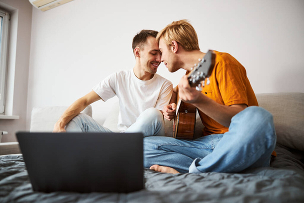 Ευτυχισμένο γκέι ζευγάρι κάθεται στο κρεβάτι και αγγίζει τα μέτωπα - Φωτογραφία, εικόνα