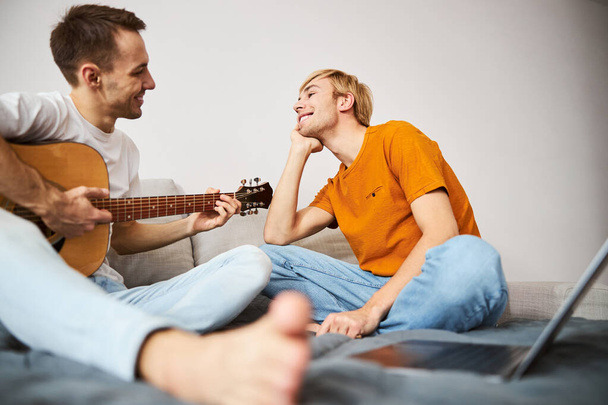 Vrolijke jongeman kijken hoe vriendje spelen gitaar - Foto, afbeelding