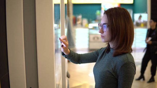 Egy fiatal nő ételt rendel az érintőterminálnál egy bevásárlóközpontban. Modern technológia. A kajáldában, sorban állás nélkül. - Fotó, kép