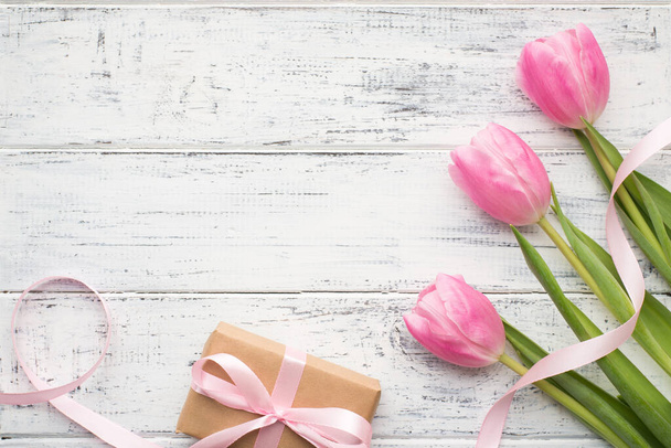 Feliz concepto del Día Internacional de la Mujer. Foto de bonitos tulipanes con tierna cinta rosa y envueltos en caja de regalo de papel kraft en escritorio de madera con espacio vacío - Foto, imagen