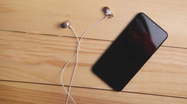 Smartfon i słuchawki na drewnianym tle. - Zdjęcie, obraz