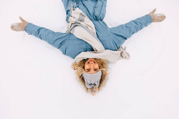 Jovem alegre, deitada na neve, fazendo um anjo da neve, sorrindo. - Foto, Imagem