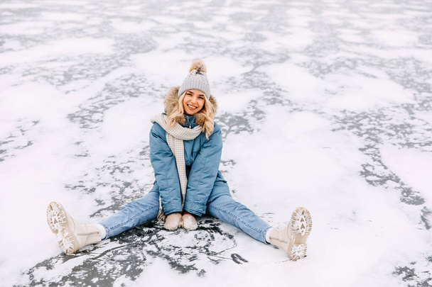 Молода блондинка сидить на льоду на замерзлому озері, в холодний зимовий день, посміхаючись, дивлячись на камеру
. - Фото, зображення