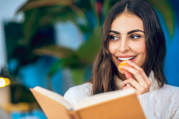 Young beautiful woman eating mandarin and smiling - Photo, image