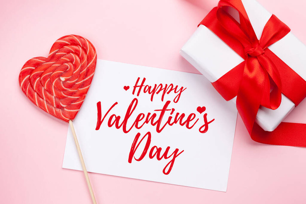 Valentines day greeting card. Gift box and heart candy lollipop over pink background. Top view flat lay - Fotografie, Obrázek