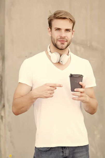Make your go-to coffee order. Handsome man point at coffee cup outdoors. Young guy drink coffee in morning. New technology. Modern life. Enjoying coffee and music - Foto, Imagen