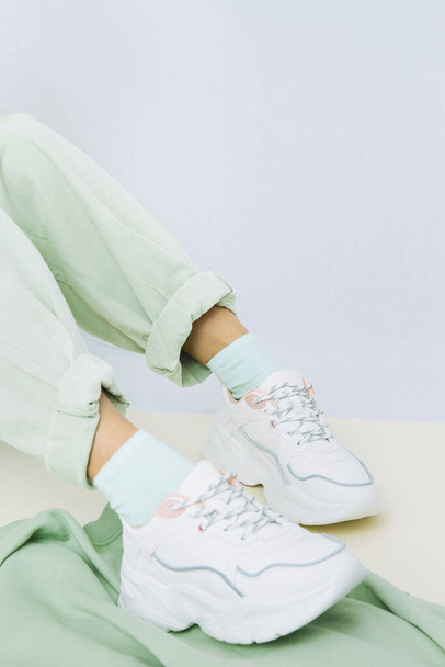 Λεπτομέρειες της trendy casual καλοκαιρινό φρέσκο ντύσιμο. Κορίτσι στο στούντιο με χακί τζιν και κομψά λευκά sneakers. Χωρίς πρόσωπο. Minimalist vegan ενδυμασία - Φωτογραφία, εικόνα