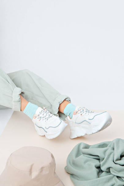 Details of trendy casual spring summer fresh outfit. Girl in studio wearing khaki jeans and stylish white sneakers.  Bucket hat and sweater. No face. Minimalist vegan clothing concept - Photo, Image