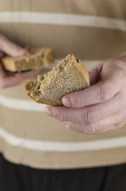 A mão de um homem estende meia fatia de pão de centeio para a câmara. No fundo, a mão segura a outra metade da fatia de pão. Misericórdia, doação, generosidade. Vista frontal. - Foto, Imagem