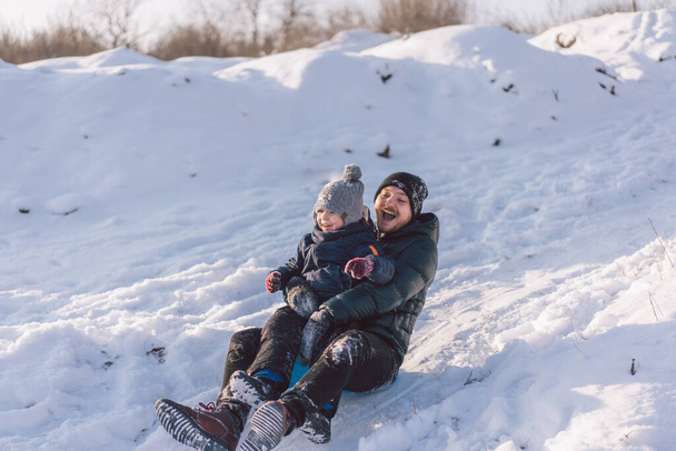 Happy dad and little boy playing with snow sled. Father and son sledding during winter holiday. - Photo, Image