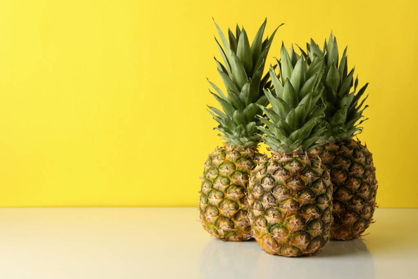 Three tasty ripe pineapples against yellow background - Foto, afbeelding