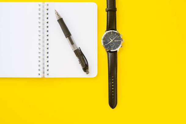 Блокнот з кільцевим зв'язувачем з ручкою наручний годинник зі шкіряними ремінцями, ізольований на жовтому тлі з копіювальним простором. Концепція письма і часу
. - Фото, зображення