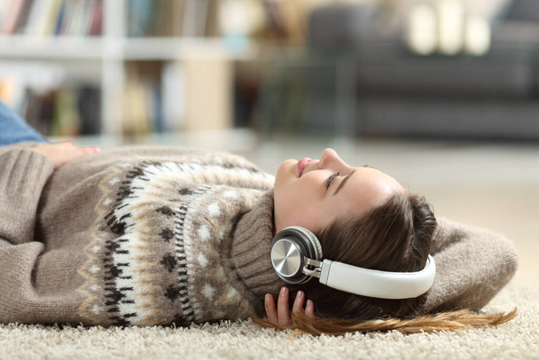 Relajado adolescente escuchando música con auriculares acostados en casa en invierno - Foto, imagen
