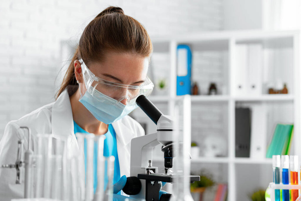 Young woman scientist using microscope in laboratory - Фото, изображение
