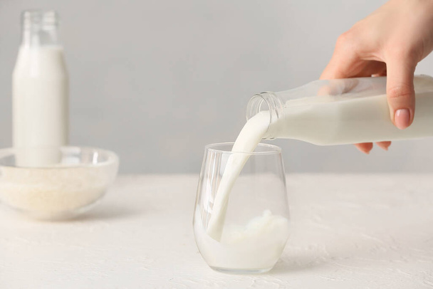 Mujer vertiendo leche de arroz de la botella en un vaso sobre la mesa - Foto, imagen