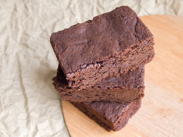 Köstlicher hausgemachter Schokoladenkuchen. Auf einem ruhigen beigefarbenen Hintergrund stapeln sich drei Stücke Brownie in einem Haufen. Einfaches und schmackhaftes Dessert. - Foto, Bild