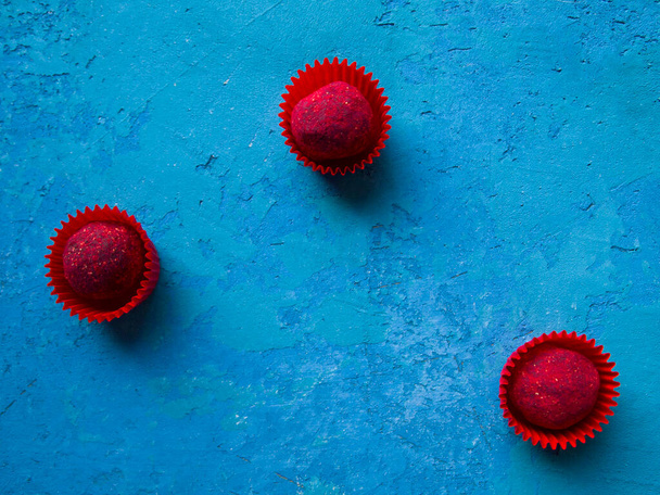 Três trufas de chocolate vermelho em fundo de concreto azul rico. Doces cobertos com framboesa sublimada. - Foto, Imagem
