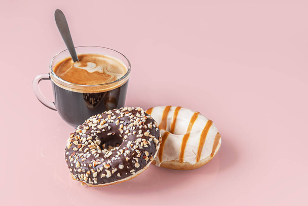 frisch gebackene Schokolade und Karamell-Donuts und eine Tasse Kaffee auf einer rosafarbenen Glasoberfläche - Foto, Bild