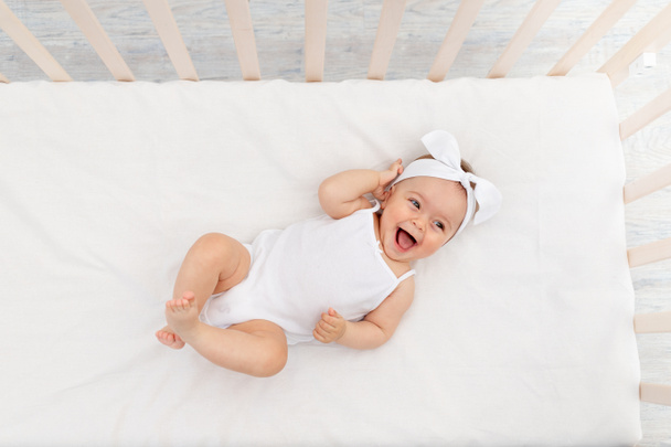 happy baby is lying in a crib in the children's room on a white bed - Foto, Imagen