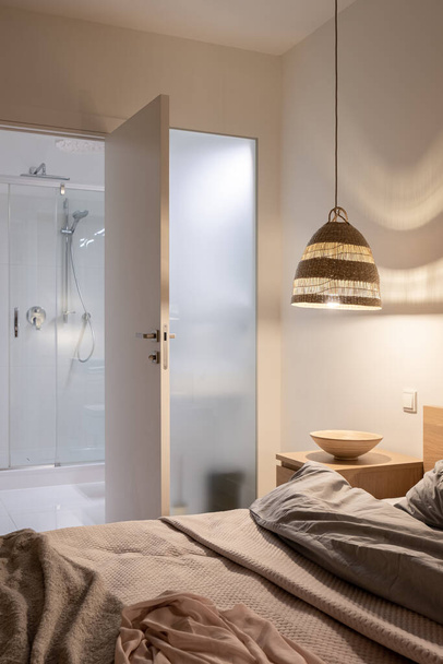Stylish and comfortable bedroom with lights on and open doors to bathroom with shower - Foto, Bild