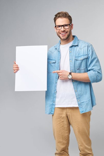 Portrait of a happy handsome young man holding blank white card or sign over white background - Foto, Imagen