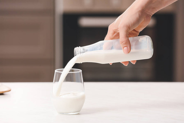 Женщина наливает рисовое молоко из бутылки в стакан на стол - Фото, изображение