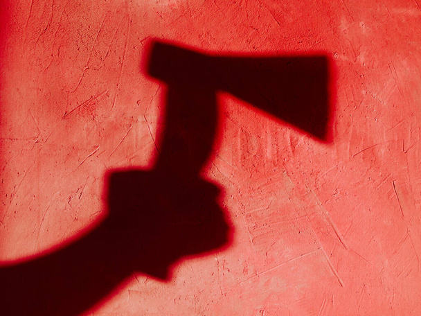 Shadow of a human hand (female or male) holding an ax on a red background. Criminal theme: possible murder. A terrible, frightening atmosphere. The outline of the shadow is highlighted in blood red. - Photo, Image