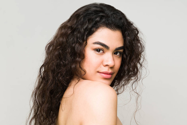 Female model with long curly hair, clean perfect skin and nude shoulders. Portrait of a young woman in a beauty spa  - Foto, Imagem