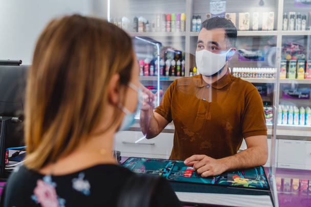 Vendeur masculin et cliente portant des masques de protection dans le magasin - Photo, image