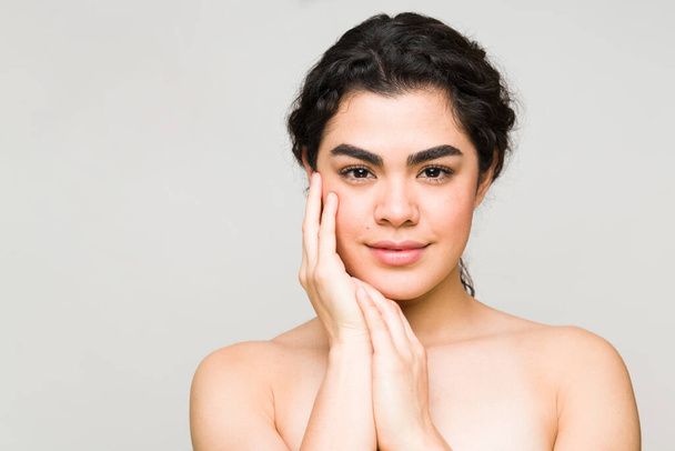 Latin young woman feeling her clean and healthy face skin after doing her daily skin care routine in the shower - Photo, Image