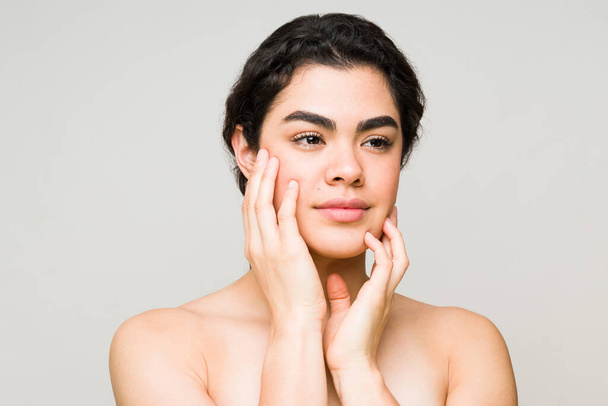 Female beauty model feeling her glowing and luminous skin after a beauty treatment at the spa. Hispanic young woman with bare shoulders - Photo, Image