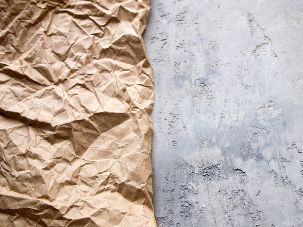 Une feuille froissée de papier artisanal marron clair repose sur une surface de béton gris. Fond abstrait avec deux textures. Espace de copie. - Photo, image