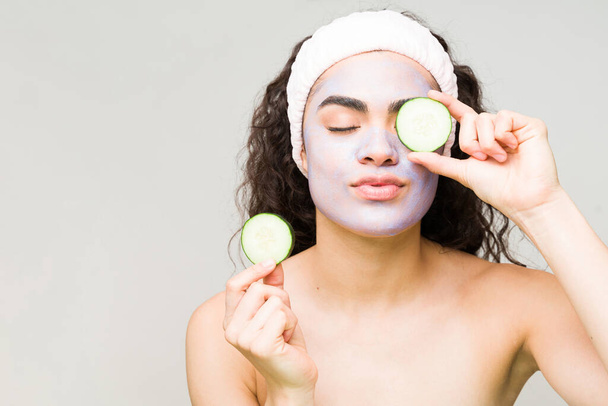 Beautiful female model putting a cucumber slice in her eyes to finish her relaxing facial treatment at the beauty spa  - Photo, Image