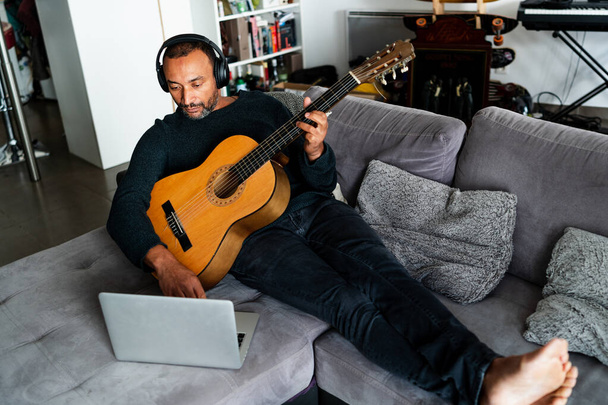 40-летний мужчина учится игре на гитаре с помощью онлайн-уроков дома - Фото, изображение