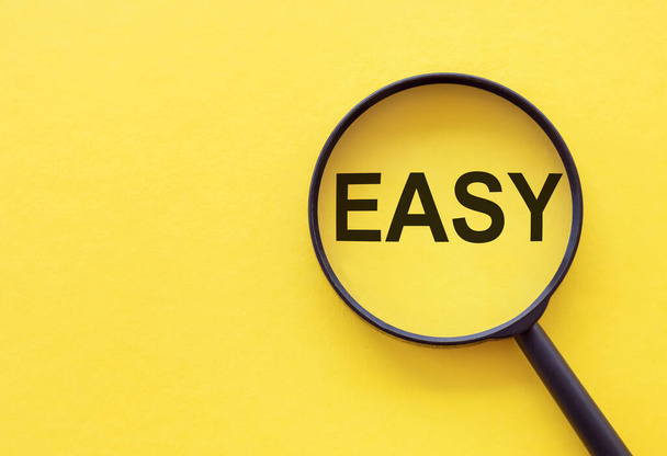 The word EASY is written on a magnifying glass on a yellow background. - Photo, Image