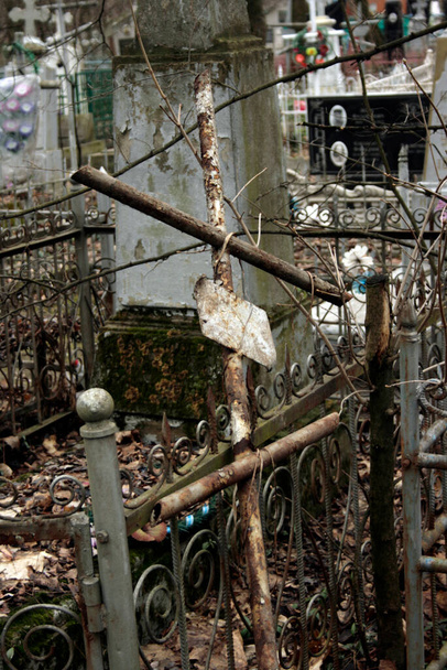 Kilátás egy elhagyatott keresztény temetőre. Egy törött fém kereszt esett a sír kerítésére. A halál és az elhagyás fogalma. - Fotó, kép